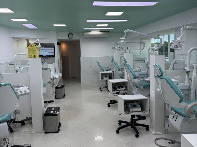 Clínica com cadeiras odontológicas lado a lado.