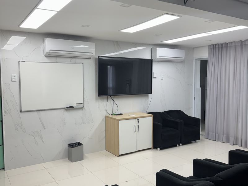 Sala de aula com quadro branco, televisão e poltronas.